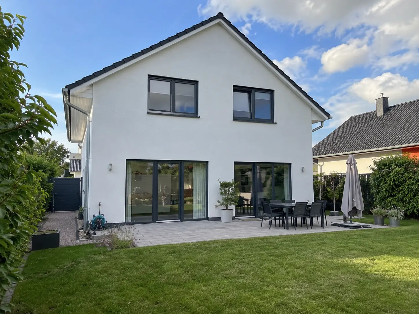 Weißes Einfamilienhaus mit Terrasse und Rasen auf der Gartenseite