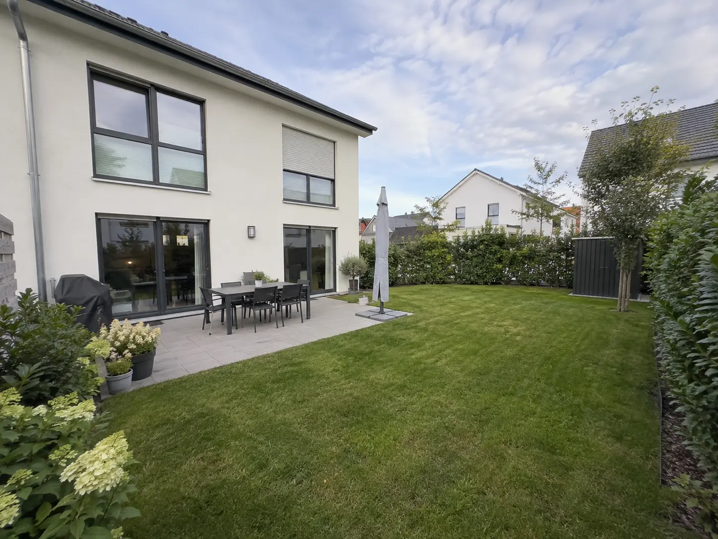 Terrasse am Haus mit Rasen und blühenden Hortensien