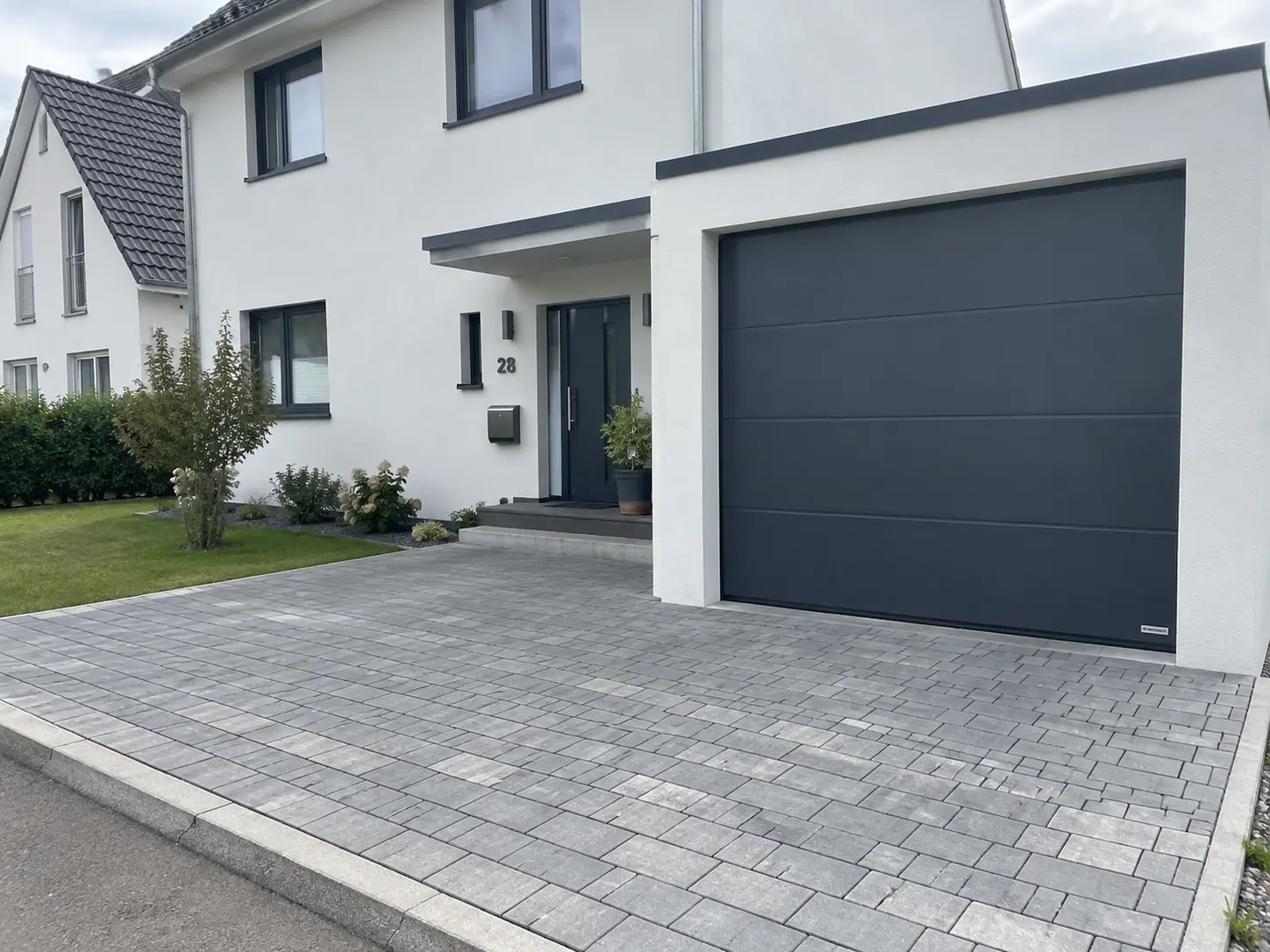 Neu gebautes Einfamilienhaus mit dunklem Garagentor und gepflasterter Einfahrt